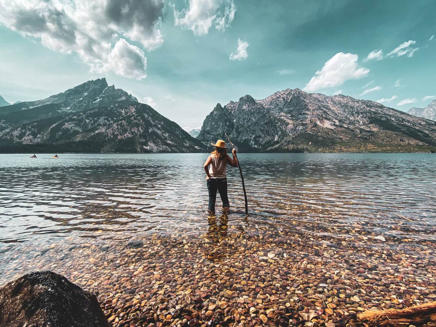 A lone traveler in the still water of an alpine lake before towering mountains